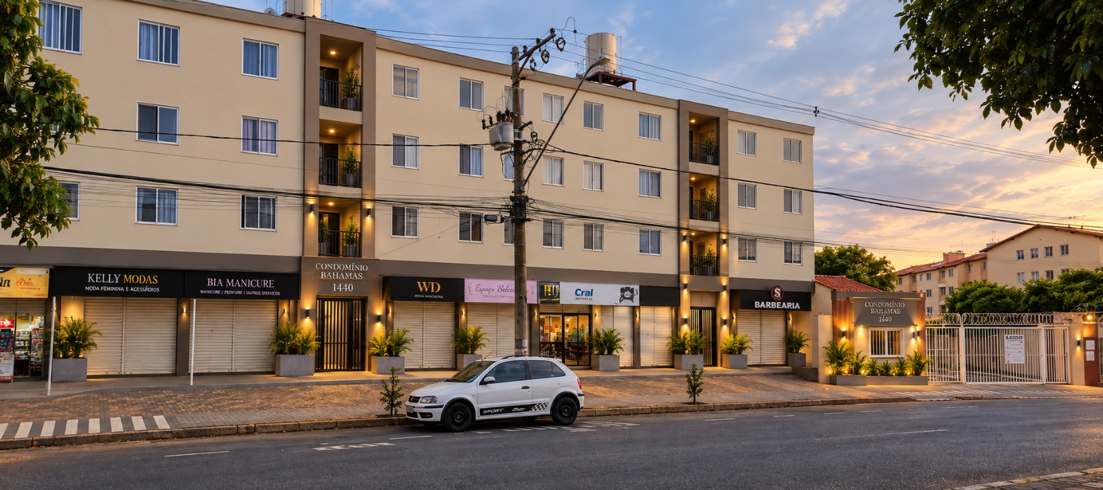 Fachada real do Condomínio Bahamas 1440 ao entardecer, com lojas iluminadas no térreo
